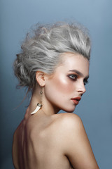 Back portrait of a young woman with bare shoulders, having a hair styling carving an impressive makeup, isolated on a blue background.