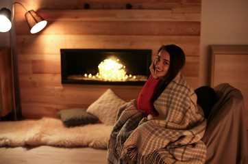 Poster - Young woman resting near decorative fireplace at home. Winter season