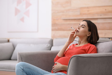 Poster - Young pregnant woman smoking cigarette at home. Space for text