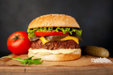 Fototapeta  - Homemade hamburger with lettuce, tomato, cheese and cucumber on a cutting board