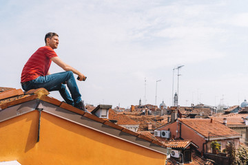 Wall Mural - young man sitting on the rooftop in venice exploring the city from above. roofing.