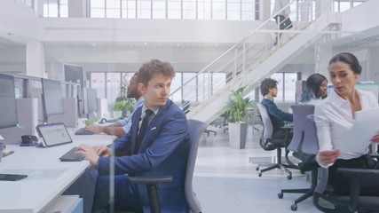 Wall Mural - Young Handsome Manager Wearing a Suit and Tie Discusses Work with his Beautiful Colleague Specialist. Diverse and Motivated Business people Work on Computers in Modern Open Office.