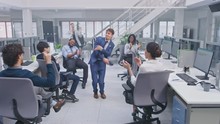Young Happy Business Manager Wearing A Suit And Tie Dancing In The Office. Colleagues Are Cheering. Diverse And Motivated Business People Work On Computers In Modern Open Office.