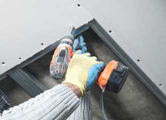 Poster - Worker with a drill screwdriver twists the screw into the drywall.