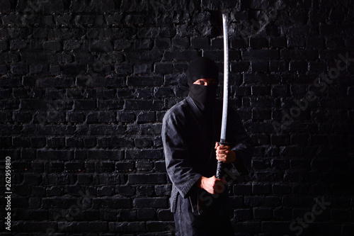 Принти на полотні Ninja samurai with katana in attack pose on a dark brick wall background