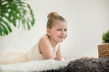 Wall Mural - Little girl in white dress lays on the floor on fur plaid in scandinavian style interior