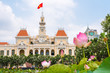 Saigon City Hall with pink lotus flowers (blurred) and blooming plumeria trees in the foreground. One of the top tourist attractions of the city of Ho Chi Minh City, Vietnam.