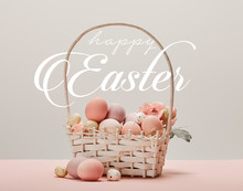 Wicker Basket With Pink Painted Eggs, Flowers And Happy Easter White Lettering On Grey Background