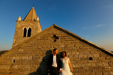 Wall Mural - Happy wedding couple posing in sun in front of old church