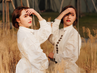 Beautiful young brunette woman in white shirt posing outdoor in front of mirror. Outdoor fashion portrait of glamour Chinese cheerful stylish girl, emotions, people, beauty and lifestyle concept.