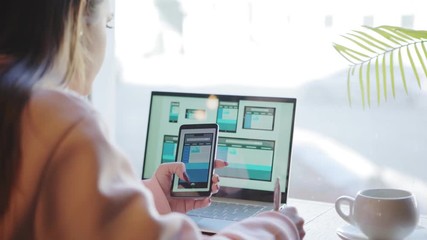 Wall Mural - Over the shoulder view of female website designer creating templates and checking it for different devices on laptop and smartphones screens 