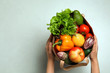 Woman holding paper bag with fresh vegetables and fruits on light background, top view. Space for text