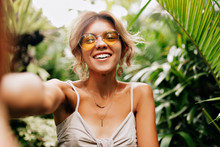 Young Caucasian Pretty Woman Wearing Yellow Round Glasses Making Selfie With Happy Smile On Background Exotic Plants  