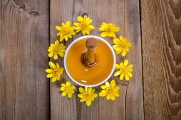 Wall Mural - honey in the glass bowl, dipper and yellow flowers around it on wooden background