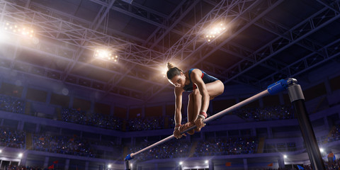 Wall Mural - Female athlete doing a complicated exciting trick on horizontal gymnastics bars in a professional gym. Girl perform stunt in bright sports clothes