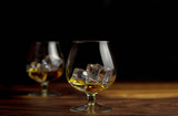 Fototapeta Lawenda - Two whiskey / cognac glasses with ice on a wooden background. Dark backdrop.