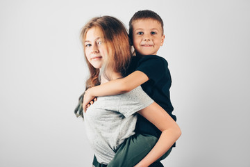 Happy kids smiling on gray background. Cute little boy on a piggy back ride with his teen sister.