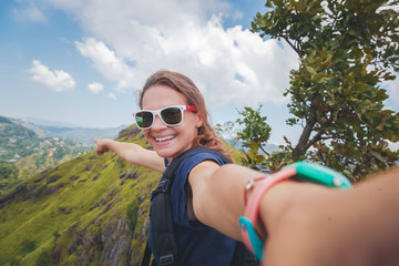 Young happy beautiful girl tourist makes selfie on the phone against the backdrop of a mountain landscape on a summer day