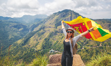 Young Happy Beautiful Woman Tourist With The Sri Lankan Flag In Her Hands Against The Backdrop Of The Mountain Landscape On A Summer Day. Travel To Sri Lanka, Island Of Ceylon