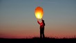 © MEDIAIMAG - Little child holds lightning chinese sky lantern and release it on red sunset sky, happy kid jumping for free dreams, conceptual