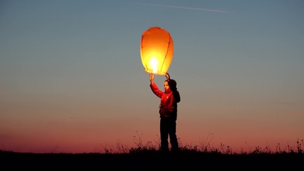 Little child holds lightning chinese sky lantern and release it on red sunset sky, happy kid jumping for free dreams, conceptual