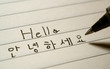 Beginner Korean language learner writing Hello word Annyeonghaseyo in Korean characters on a notebook