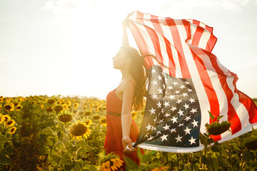 Beautiful girl with the American flag in a sunflower field. 4th of July. Fourth of July. Freedom. Sunset light The girl smiles. Beautiful sunset. Independence Day. Patriotic holiday.