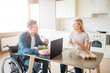 © estradaanton - Happy cheerful young student with disability and inclusiveness eating salad and studying. He look at woman and smile. She cooks. Happy couple sit together in kitchen.