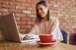 © Dusan Petkovic - Close up of fresh espresso in red cup. In background woman typing on report on laptop.