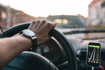 Wall Mural - driver with a wristwatch rides through the city using a navigator on a smartphone on a sunny day.