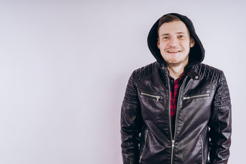 Wall Mural - Man in trendy jacket on white background. Portrait of young male in leather jacket zipping up and smiling at camera on white background