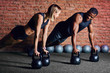 © alfa27 - Sporty young interracial couple doing plank exercise with dumbbells on red brick wall background. African cross fit instructor teaching his blonde female client to do a plank