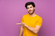 © luismolinero - Handsome over isolated purple wall presenting an idea while looking smiling towards