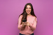 © luismolinero - Teenager girl over purple wall sending a message with the mobile