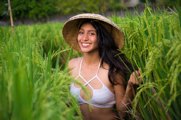 young happy and beautiful hispanic woman in traditional Asian farmer hat smiling cheerful posing sexy isolated on green rice field in Asia tourist trip and Summer holidays travel and adventure