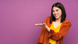 © luismolinero - Young woman with a coat over isolated purple background extending hands to the side for inviting to come