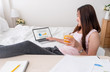 © weedezign - Asian female wear tank top siting and use laptop on bed and drink orange juice in bedroom at home.Work at home concept.work from home.relax lifestyle.
