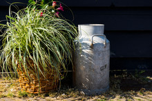 Decorative Milk Churn, Can And Flower In Wicket Bucket Against Black Wall