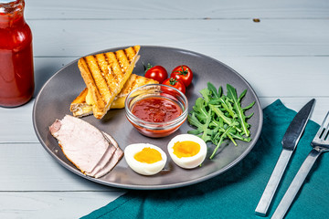 morning breakfast in a gray plate of boiled eggs, toast with cheese and vegetables on a white wooden background