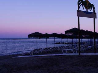 Wall Mural - Calm evening scene at a beach in Spain's resorts, Empty beds, straw umbrellas, purple colors.