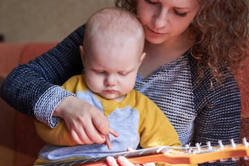 Wall Mural - Mom teaches her little son to play the guitar. Early child development.