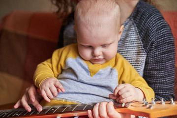 Wall Mural - Mom teaches her little son to play the guitar. Early child development.