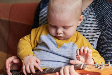 Wall Mural - Mom teaches her little son to play the guitar. Early child development.