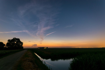 Sticker - Twilight sky over a tree and farm in the dutch landscape with reflections in the water of a canal.