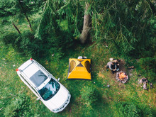 Couple Sitting Near Campfire Drinking Tea. Yellow Tent And White Suv Car