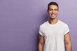© wayhome.studio  - Handsome cheerful young sportsman has sporty body, muscular arms, wears white mock up t shirt, has short dark hair, toothy appealing smile, stands over purple background, blank copy space aside