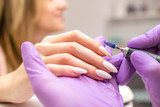 Manicurist work on a woman client hands, make her nails look beautiful. Salon procedure in process. Professional works in gloves using drill for sterility