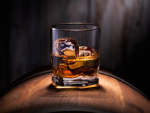 Glass Of Whiskey With Ice Cubes On The Wooden Barrel With Wooden Background