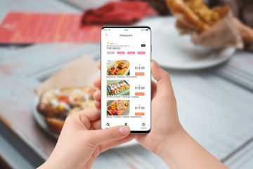 Female hand in the restaurant ordering food with app on her phone, blurred table with food in background