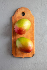 Sweet mangoes on rustic wooden board on gray surface, top view. Flat lay, from above, overhead. Close-up.